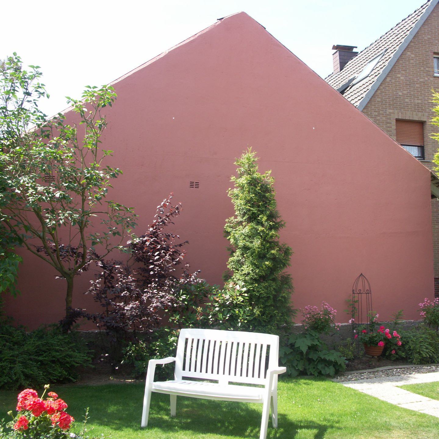 Giebelwand in Terrakotta hinter einem Garten mit weißer Bank