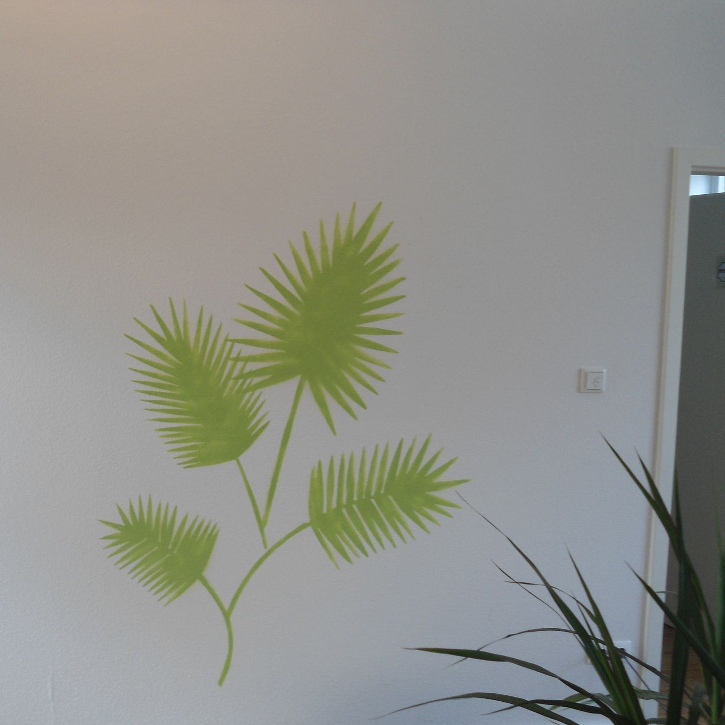 Helle Wand mit grünem Wandmotiv aus Palmenblättern